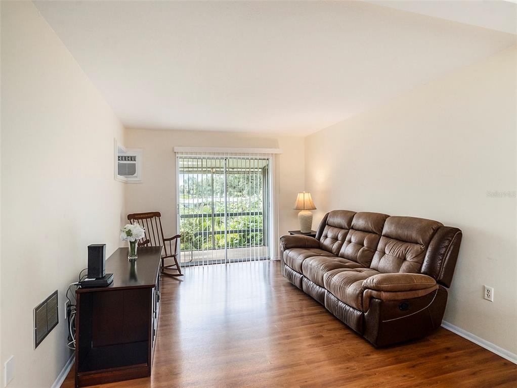 A living room features a brown leather sofa, wood flooring, and a sliding glass door — 1859 RESTFUL DRIVE UNIT L26, BRADENTON, FL