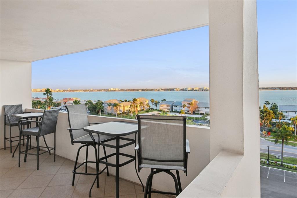 A balcony with outdoor furniture overlooks a body of water and nearby residential buildings — 1270 GULF BOULEVARD UNIT 701, CLEARWATER, FL