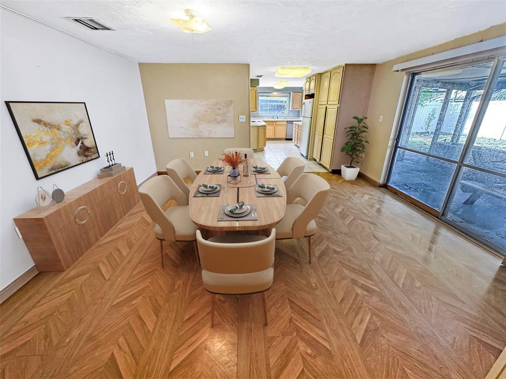 A dining room with herringbone wood floors, a central table, and an adjacent kitchen — 1815 LOWRY AVENUE, LAKELAND, FL