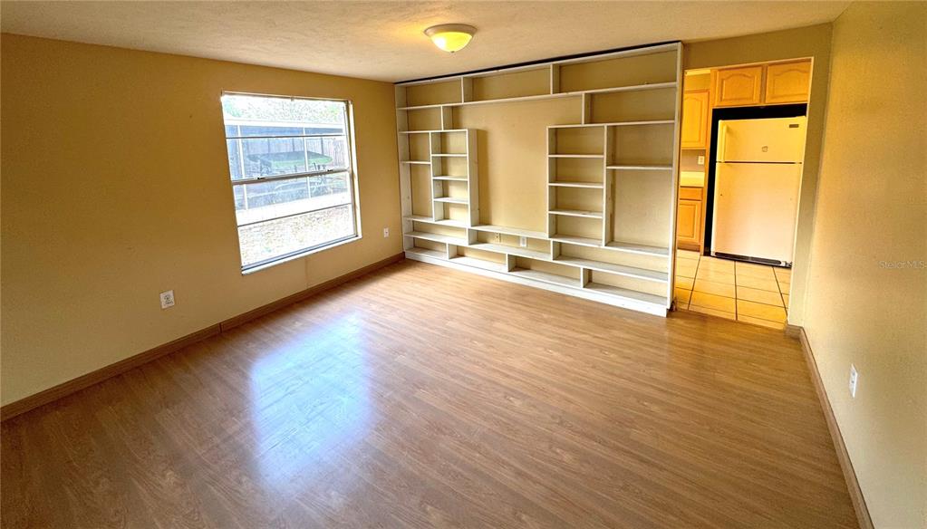 A room with wood-look flooring, a large built-in shelving unit, and a view of a kitchen — 1815 LOWRY AVENUE, LAKELAND, FL