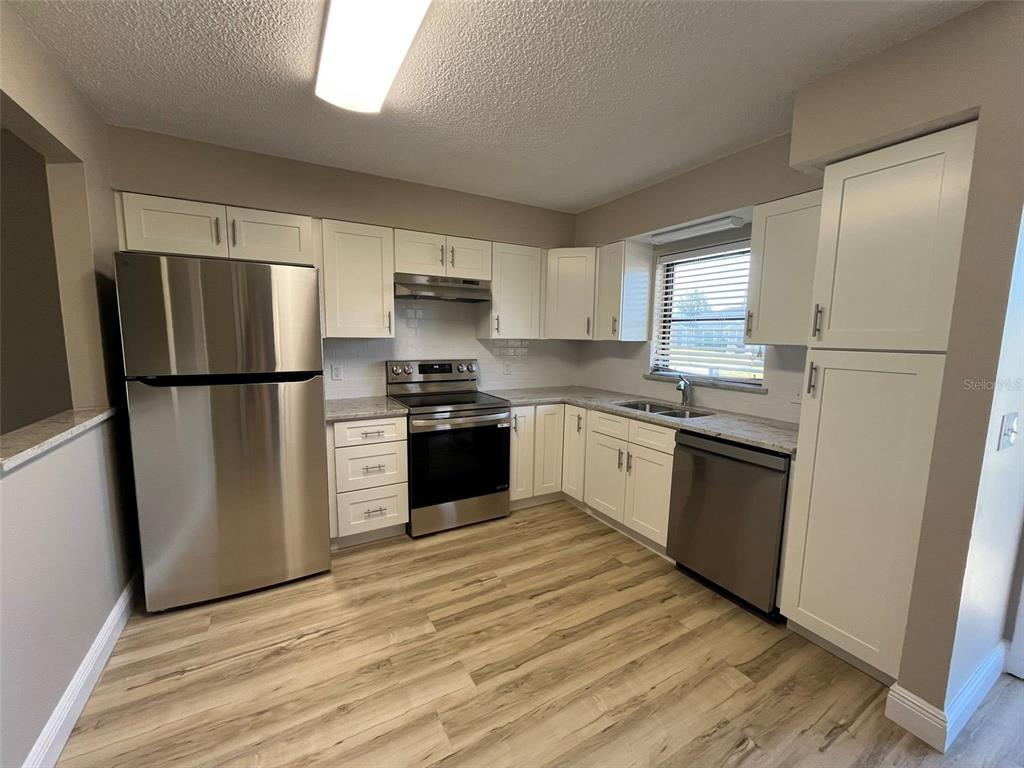 A kitchen with white cabinets, stainless steel appliances, and light wood-look flooring — 11050 PENDLETON AVENUE UNIT A, ENGLEWOOD, FL