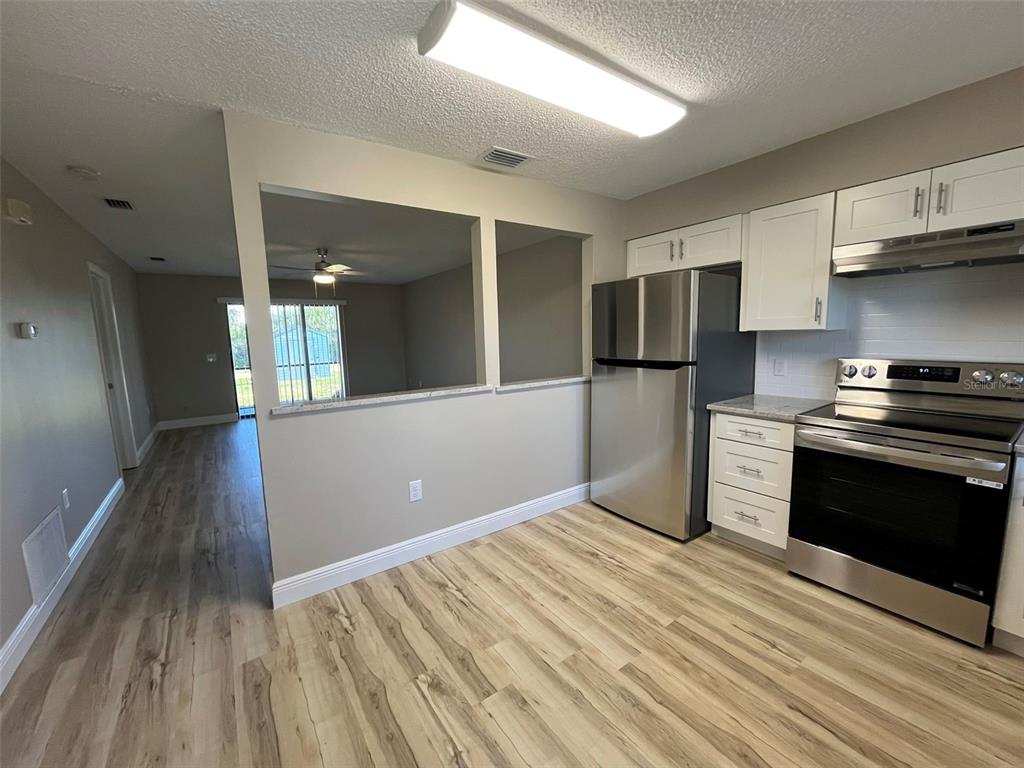 A kitchen with white cabinets, stainless steel appliances, and wood-look flooring opens to a living area — 11050 PENDLETON AVENUE UNIT A, ENGLEWOOD, FL