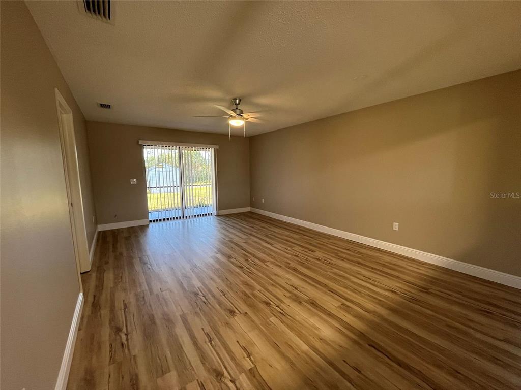 An empty room features light wood-look flooring, beige walls, and a sliding glass door — 11050 PENDLETON AVENUE UNIT A, ENGLEWOOD, FL