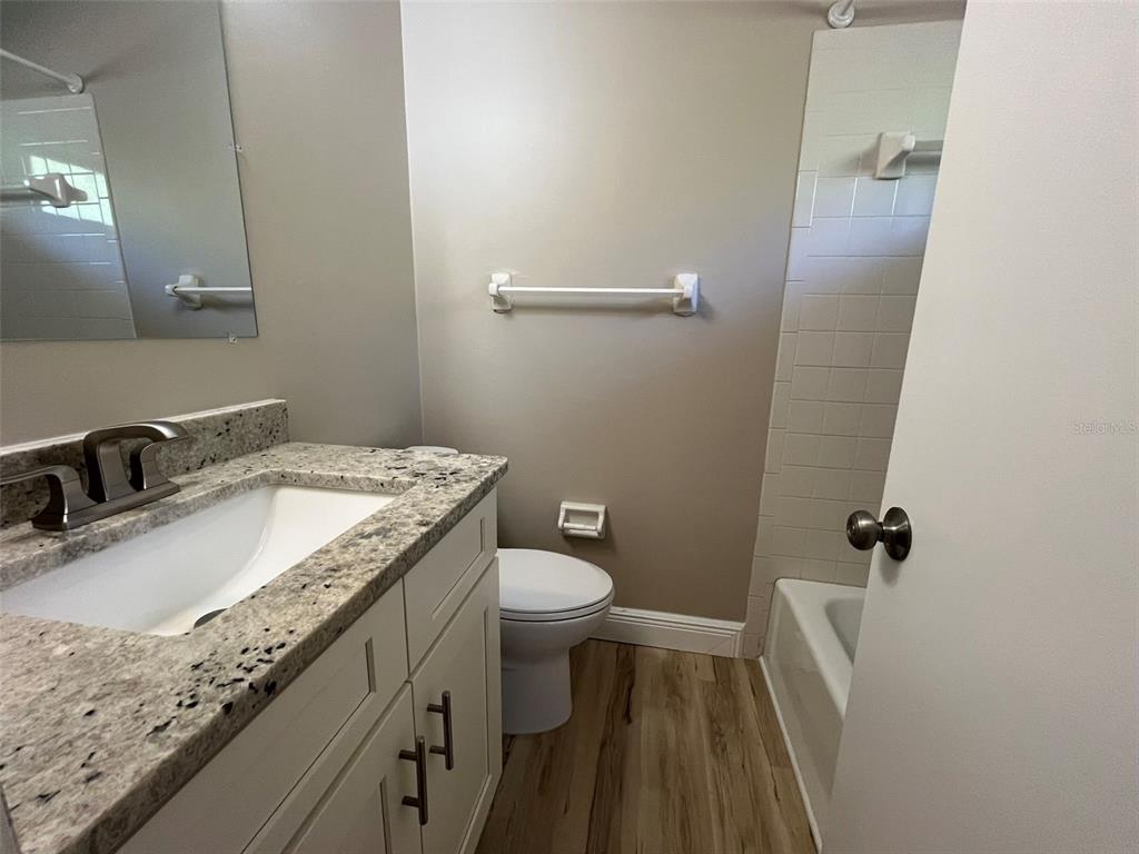 A bathroom features a granite-topped vanity, a white toilet, and a tiled shower-tub combination — 11050 PENDLETON AVENUE UNIT A, ENGLEWOOD, FL