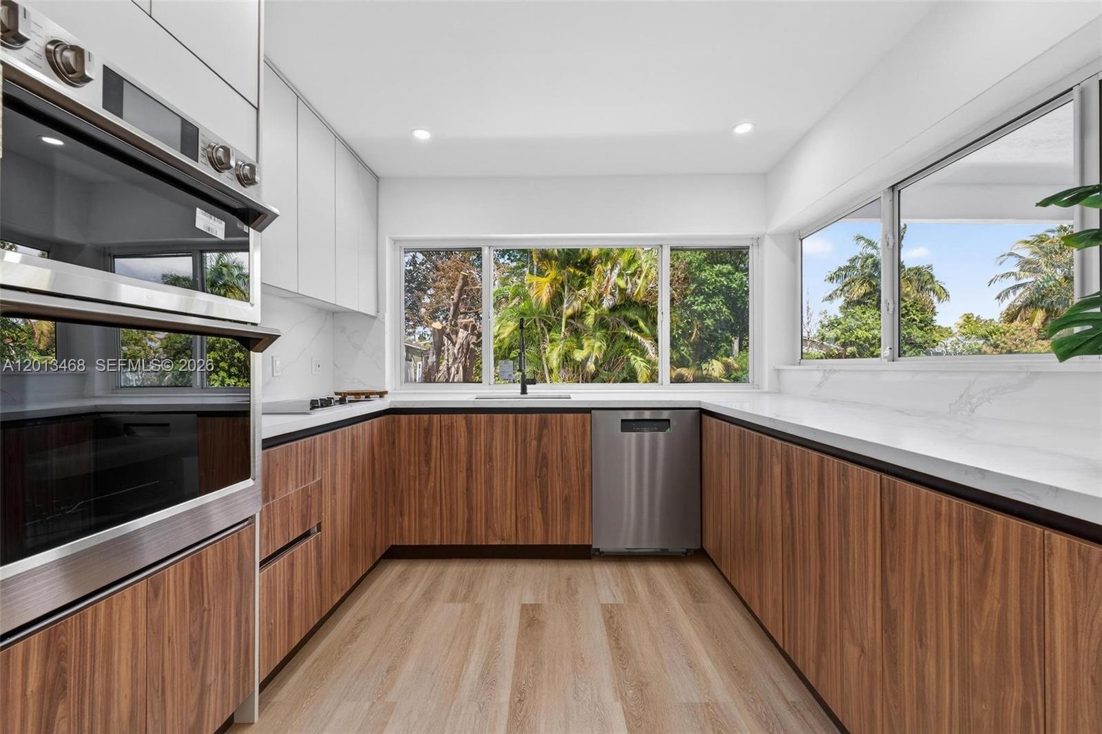 A modern kitchen features wood-grain cabinets, white countertops, stainless steel appliances, and large windows — 6621 Ficus Dr, Miramar FL 33023, MIRAMAR, FL
