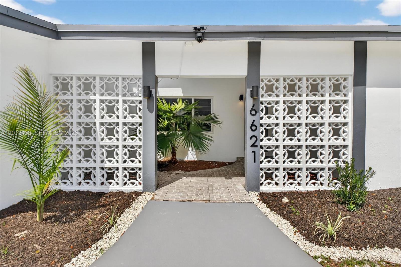 The exterior of a house features white breeze block walls, a gray walkway, and landscaping — 6621 Ficus Dr, Miramar FL 33023, MIRAMAR, FL