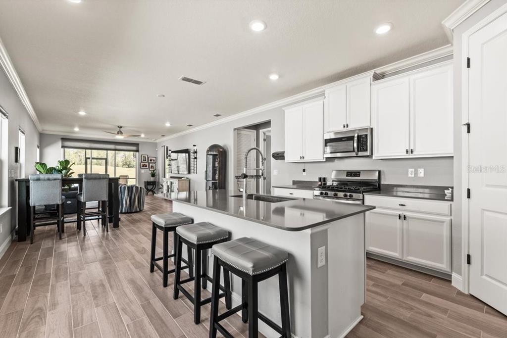 A modern kitchen features white cabinets, a gray island with bar stools, and wood-look flooring — 907 STILLWATER BOULEVARD, ST JOHNS, FL