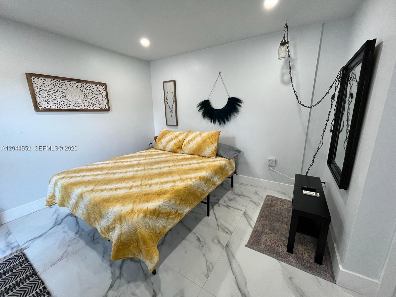 A bedroom features a yellow patterned bedspread, white marble-style tile flooring, and minimalist wall decor — MIAMI, FL