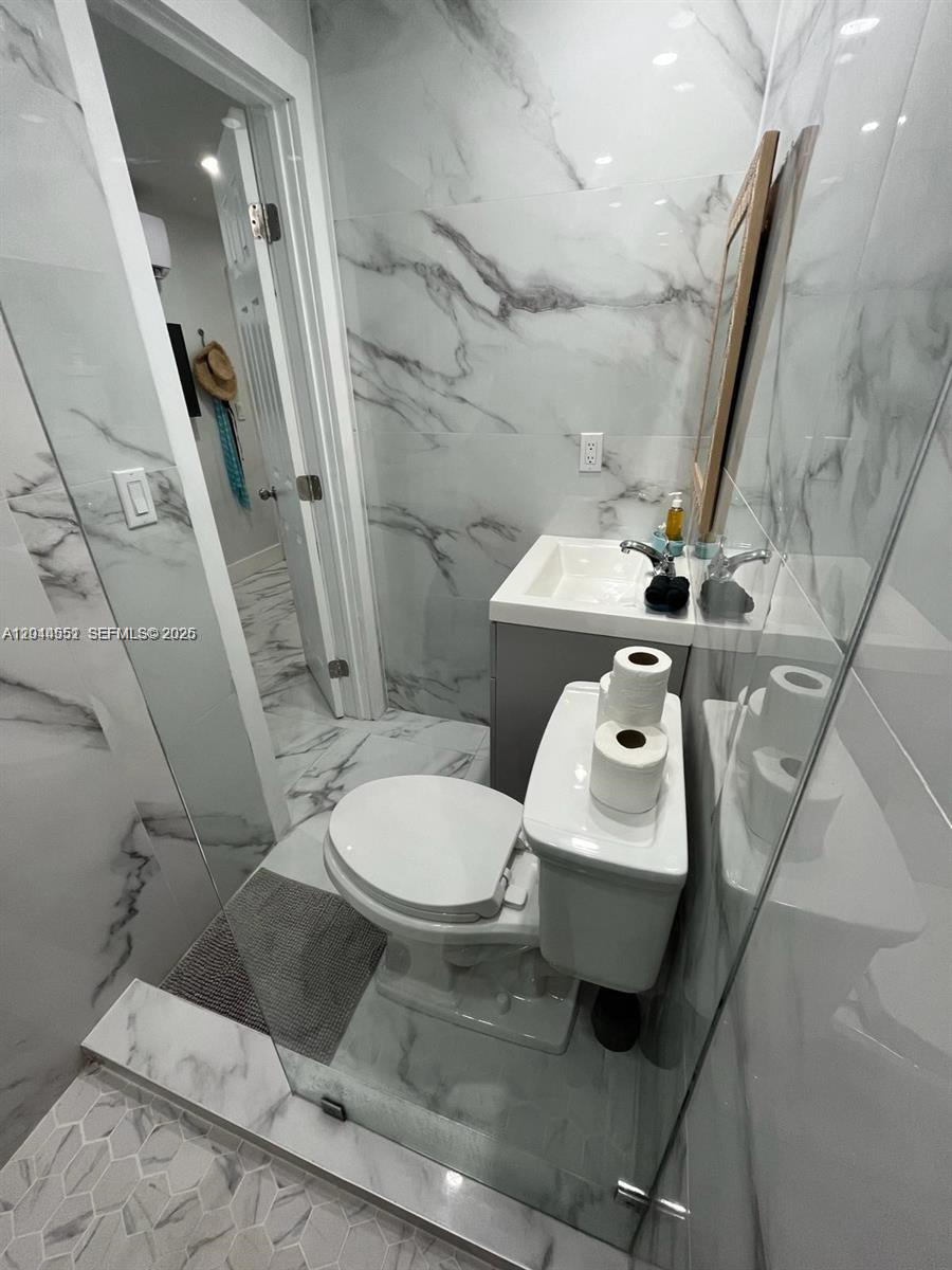 A small bathroom features marble-patterned tile walls, a white toilet, and a modern vanity — MIAMI, FL