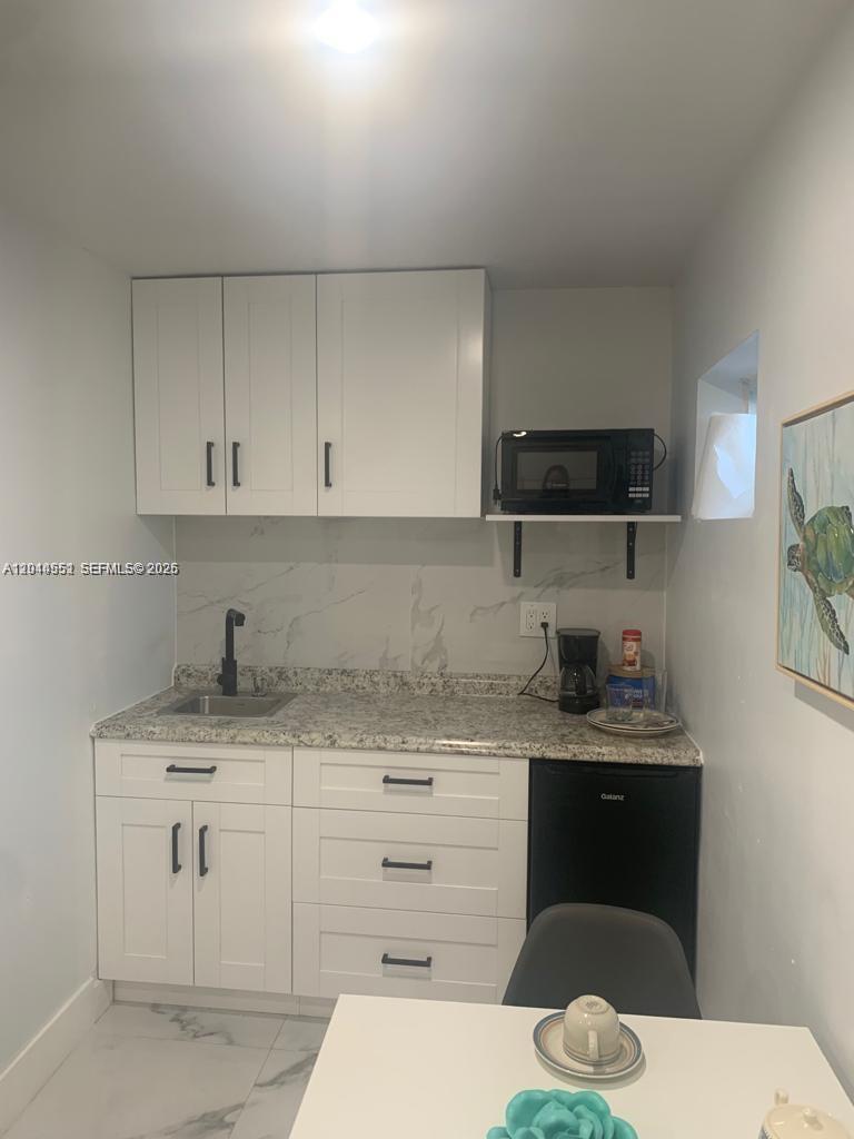 A small kitchen features white cabinets, a granite countertop, a sink, and a mini-fridge — MIAMI, FL