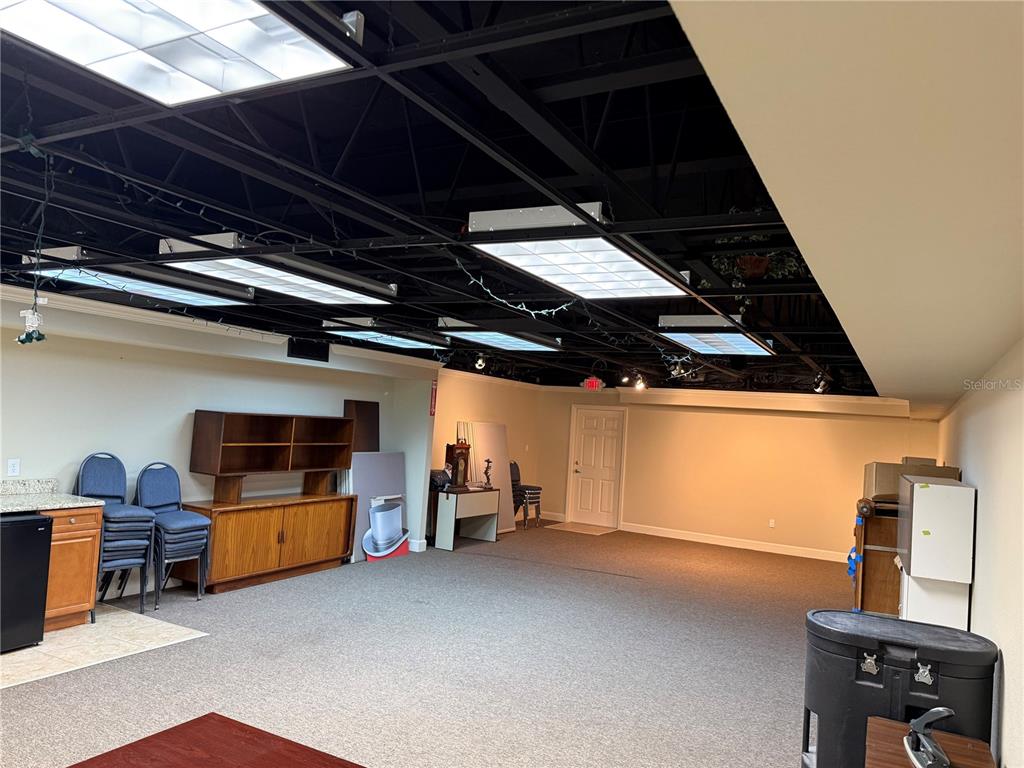 A large room with a black exposed ceiling, fluorescent lighting, and gray carpeting — 221 W STATE ROAD 434, LONGWOOD, FL