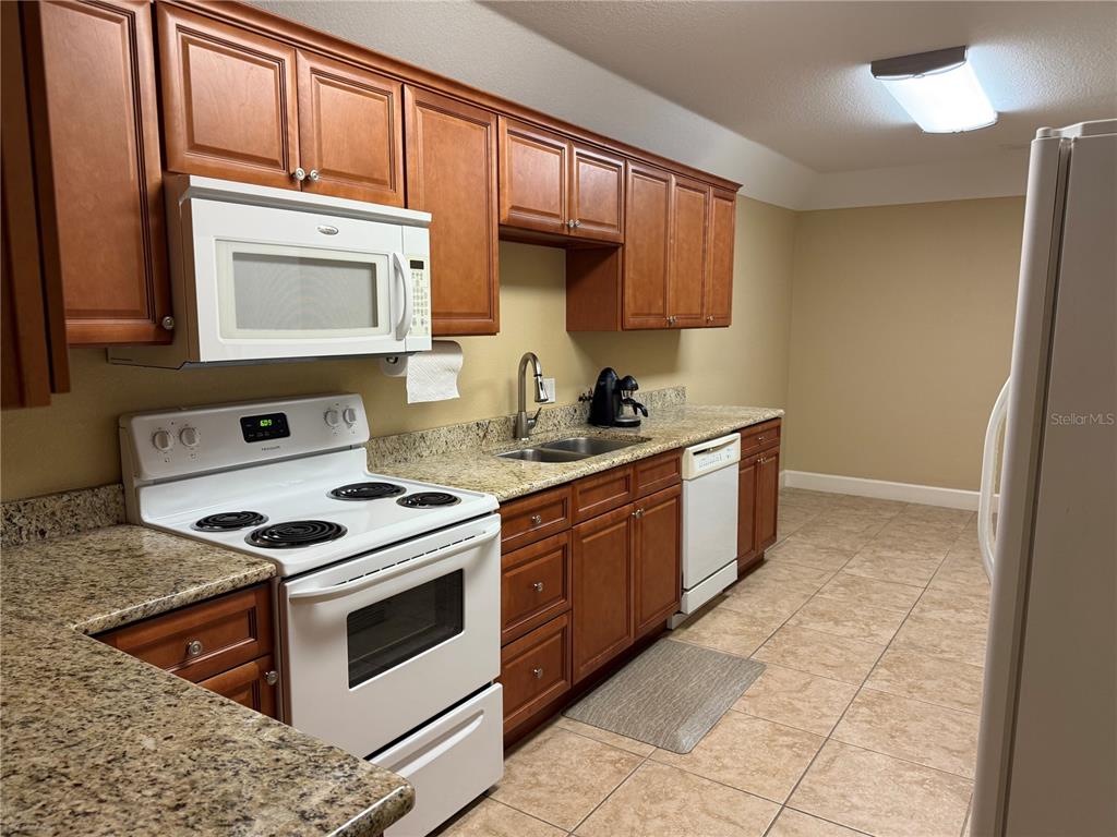 A kitchen features wood cabinets, granite countertops, white appliances, and tiled flooring — 221 W STATE ROAD 434, LONGWOOD, FL