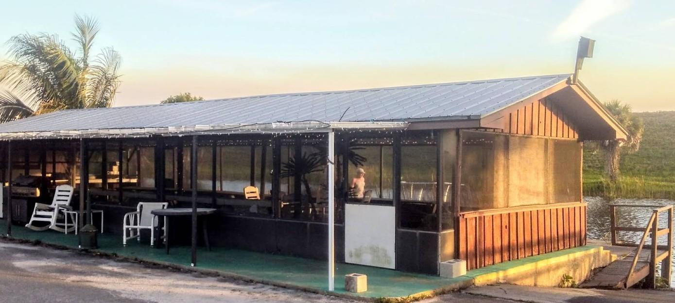 A long, screened-in wooden building with a metal roof sits beside a body of water — 4074 Hwy 441, Okeechobee FL 34971, OKEECHOBEE, FL