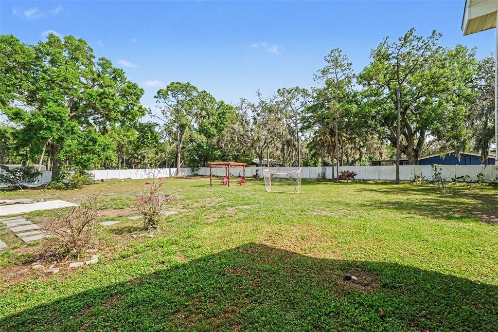 A large, grassy backyard features a white fence, a wooden pergola, and a soccer goal — 3101 S KINGS AVENUE, BRANDON, FL