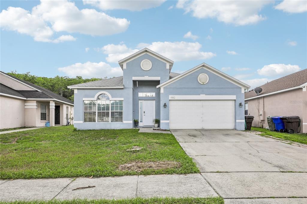 A light blue, single-story suburban house with a two-car garage and a front lawn — 1982 LOCUST BERRY DRIVE, KISSIMMEE, FL