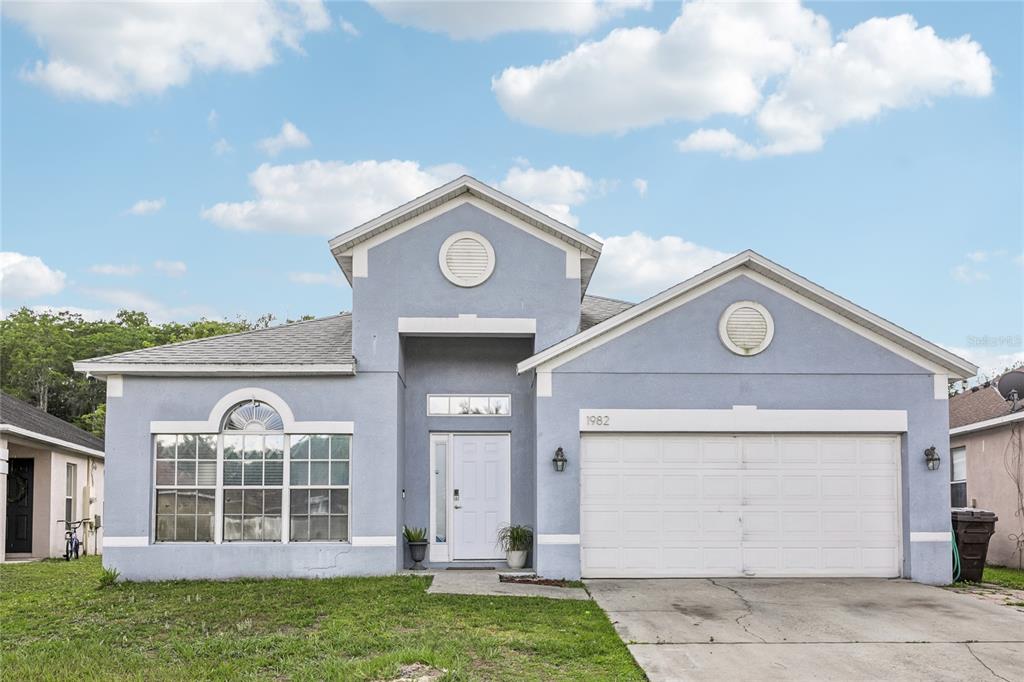 A single-story blue house with a two-car garage, arched window, and a white front door — 1982 LOCUST BERRY DRIVE, KISSIMMEE, FL