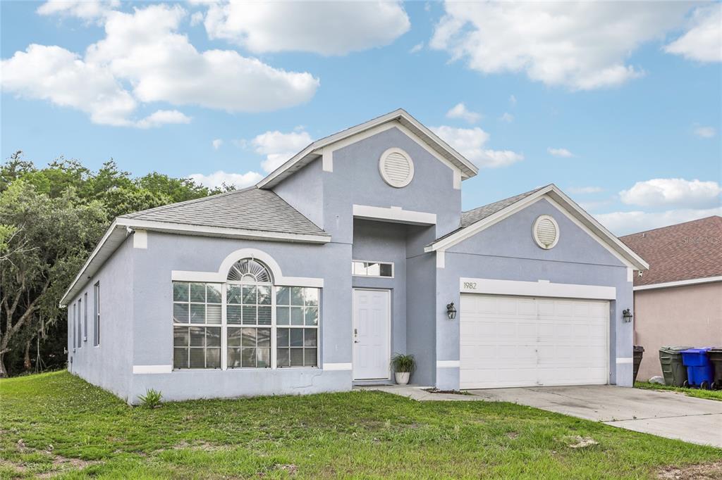 A light blue single-story house with a two-car garage and a large arched front window — 1982 LOCUST BERRY DRIVE, KISSIMMEE, FL
