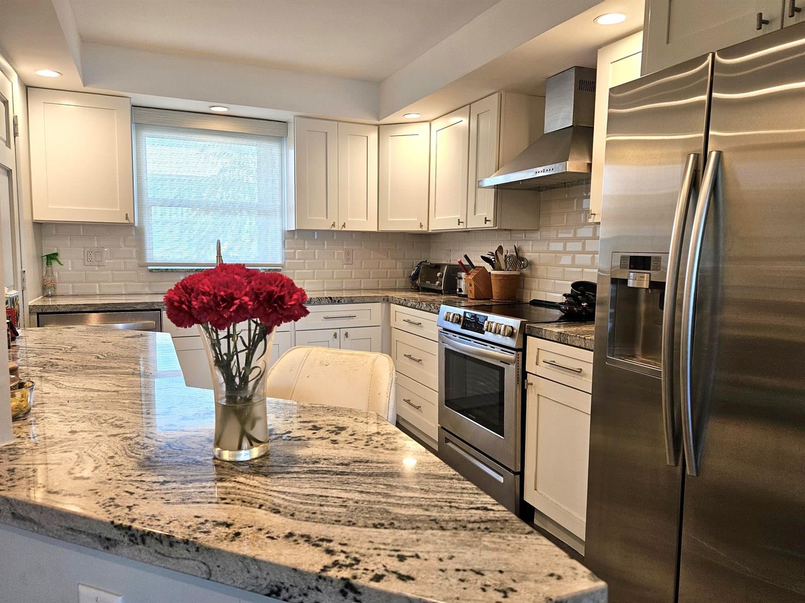 A kitchen features white cabinets, granite countertops, stainless steel appliances, and a vase of flowers — 5530 N Ocean Boulevard # 106, Ocean Ridge FL 33435, OCEAN RIDGE, FL
