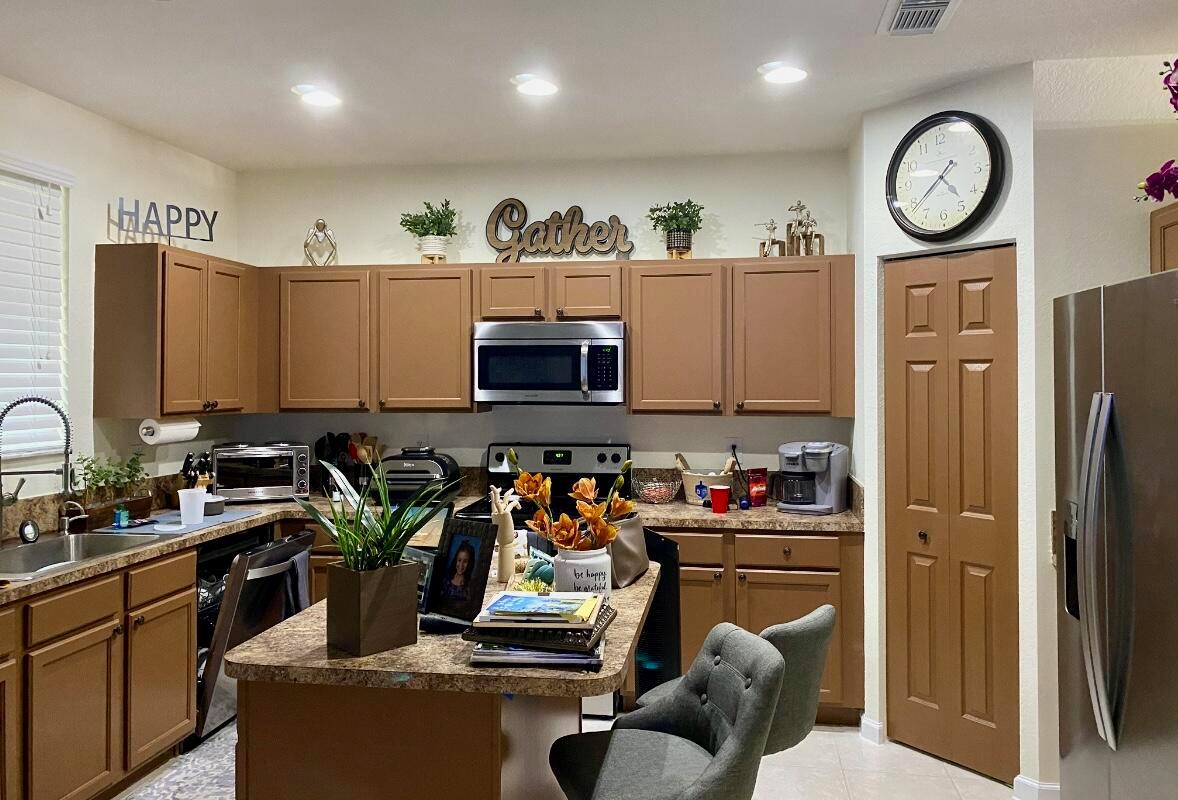 A kitchen features brown cabinets, a central island with two chairs, and a wall clock — 2823 S Evergreen Circle, Boynton Beach FL 33426, BOYNTON BEACH, FL