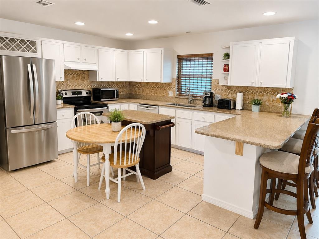 A kitchen features white cabinets, granite countertops, a center island, and a small dining table — 3430 TAMARIND DRIVE, EDGEWATER, FL