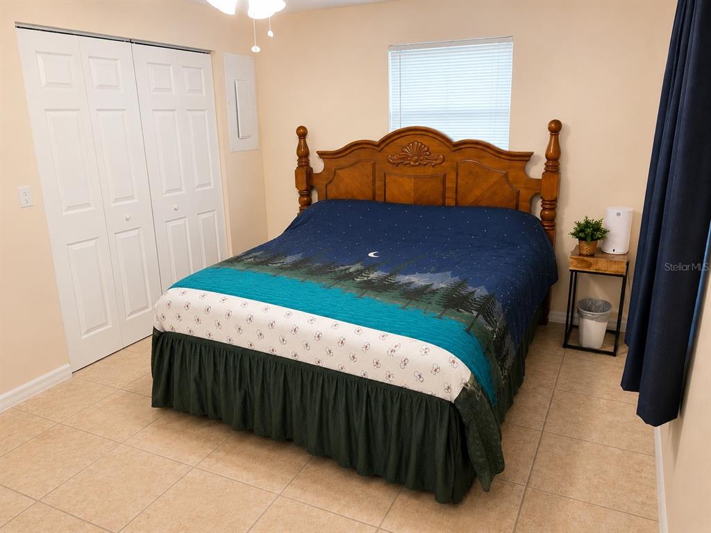 A bedroom features a wooden bed frame, a forest-themed quilt, and tile flooring — 3430 TAMARIND DRIVE, EDGEWATER, FL