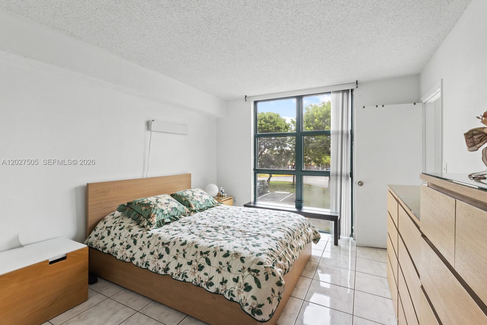 A bedroom features a bed with floral bedding, tile flooring, and a large window — 2075 SW 122nd Ave # 226, Miami FL 33175, MIAMI, FL