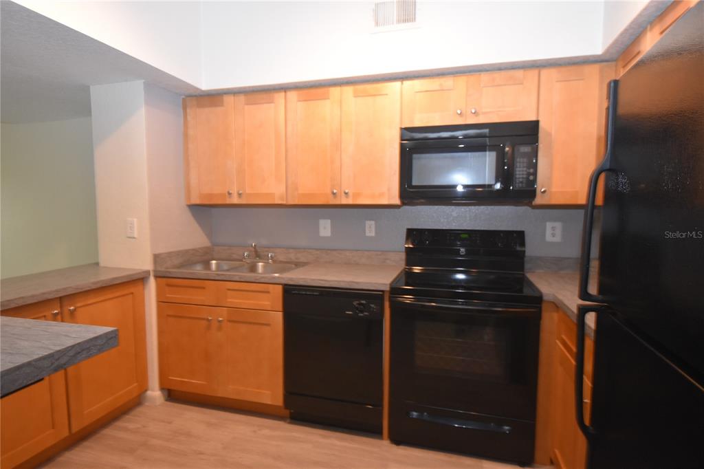 A kitchen features light wood cabinets, black appliances, a double sink, and gray laminate countertops — 2402 W AZEELE STREET UNIT 426, TAMPA, FL