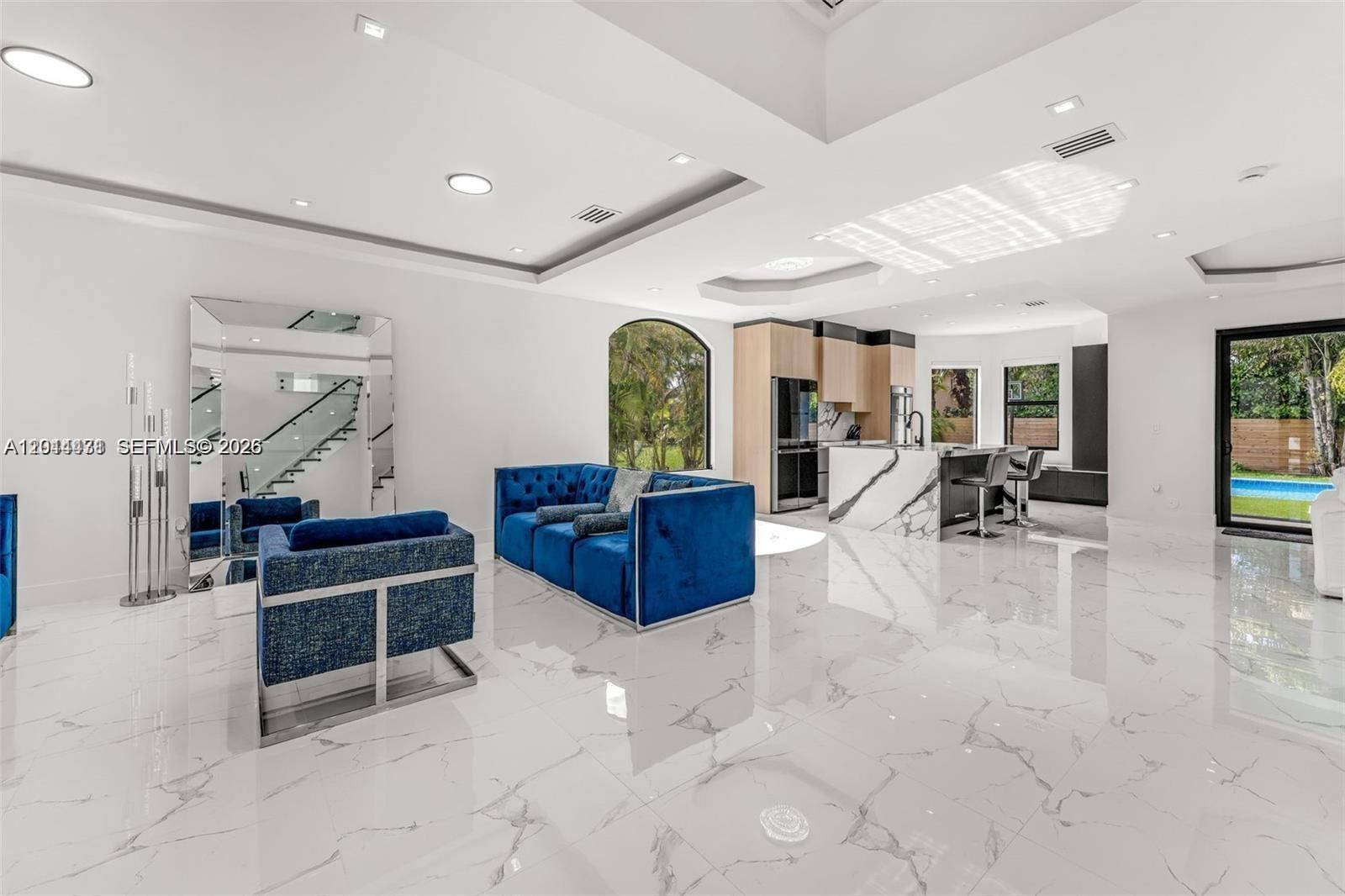 A modern open-concept living area features a blue velvet sofa, marble floors, and a kitchen — 19246 SW 132nd Ave, Miami FL 33177, MIAMI, FL