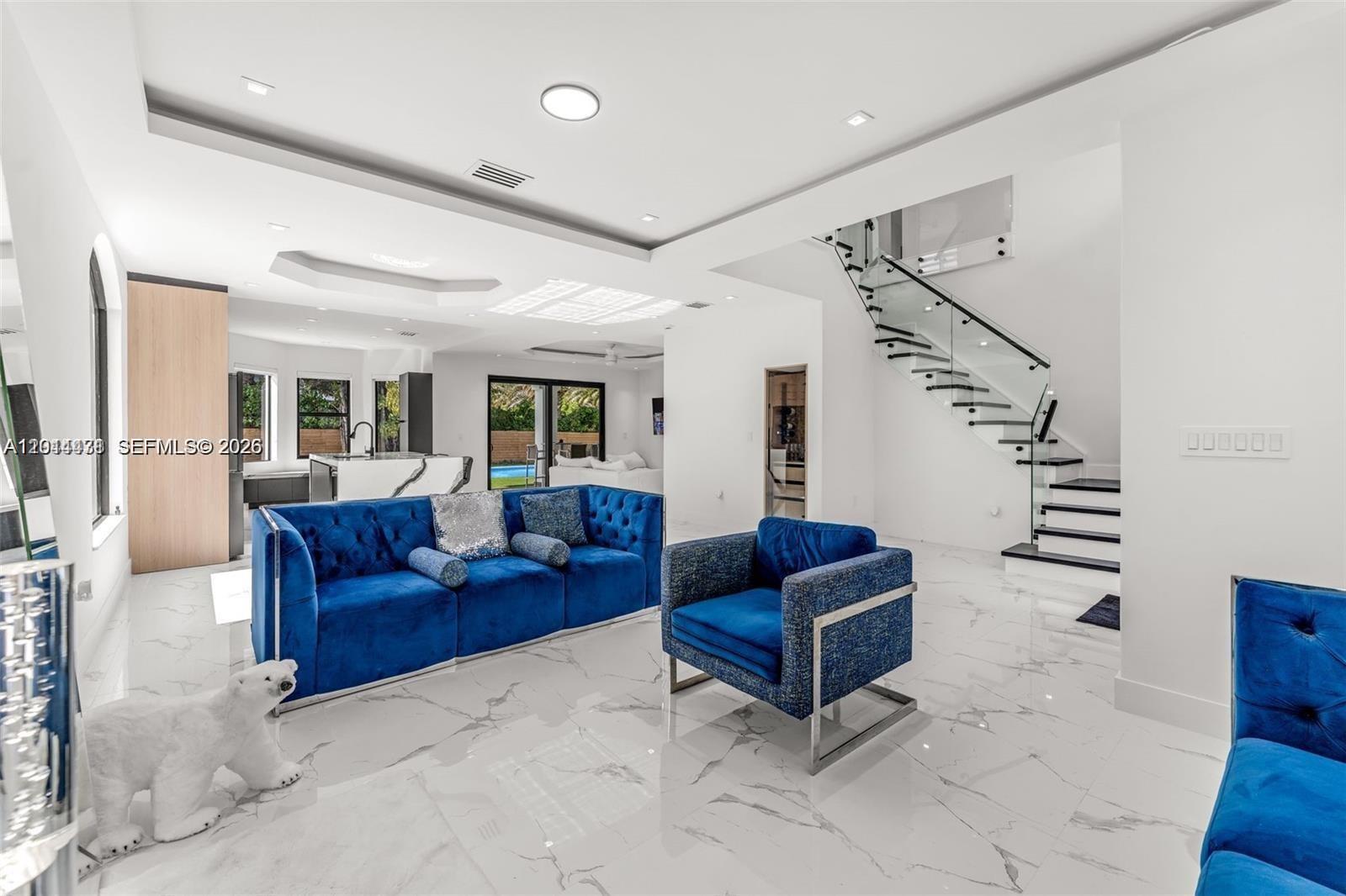 A modern living room features blue velvet furniture, marble flooring, and a glass-railed staircase — 19246 SW 132nd Ave, Miami FL 33177, MIAMI, FL