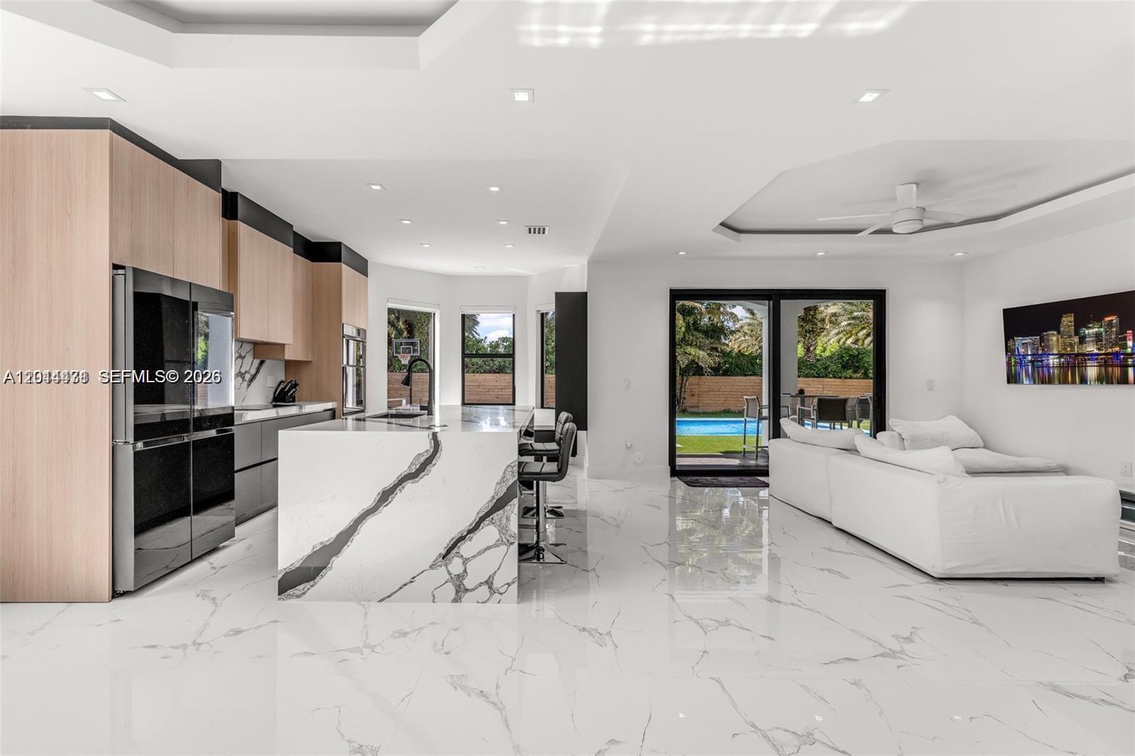 A modern open-concept kitchen and living area features marble flooring, a waterfall island, and pool views — 19246 SW 132nd Ave, Miami FL 33177, MIAMI, FL
