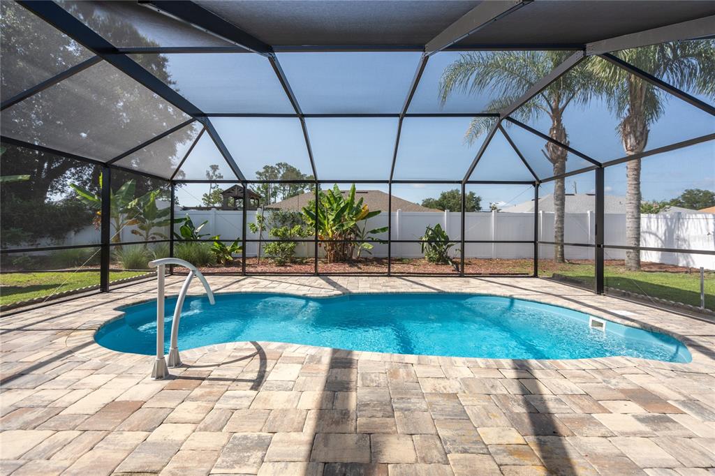 A screened-in pool patio features a blue swimming pool with pavers and a white fence — 50 ROLLING SANDS DRIVE, PALM COAST, FL