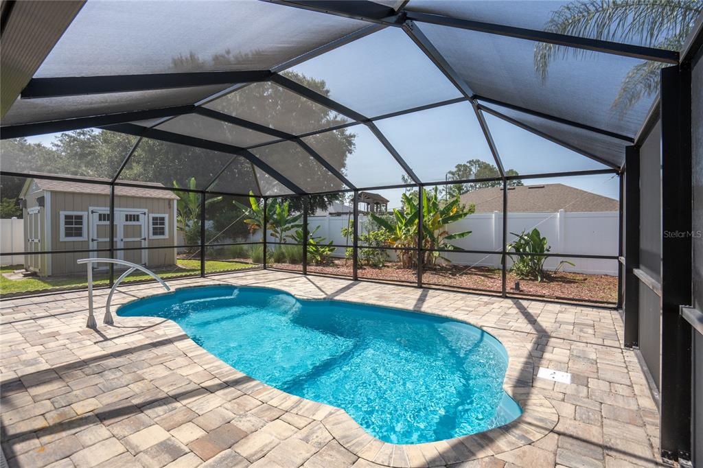 A screened-in patio features a swimming pool surrounded by stone pavers and a storage shed — 50 ROLLING SANDS DRIVE, PALM COAST, FL