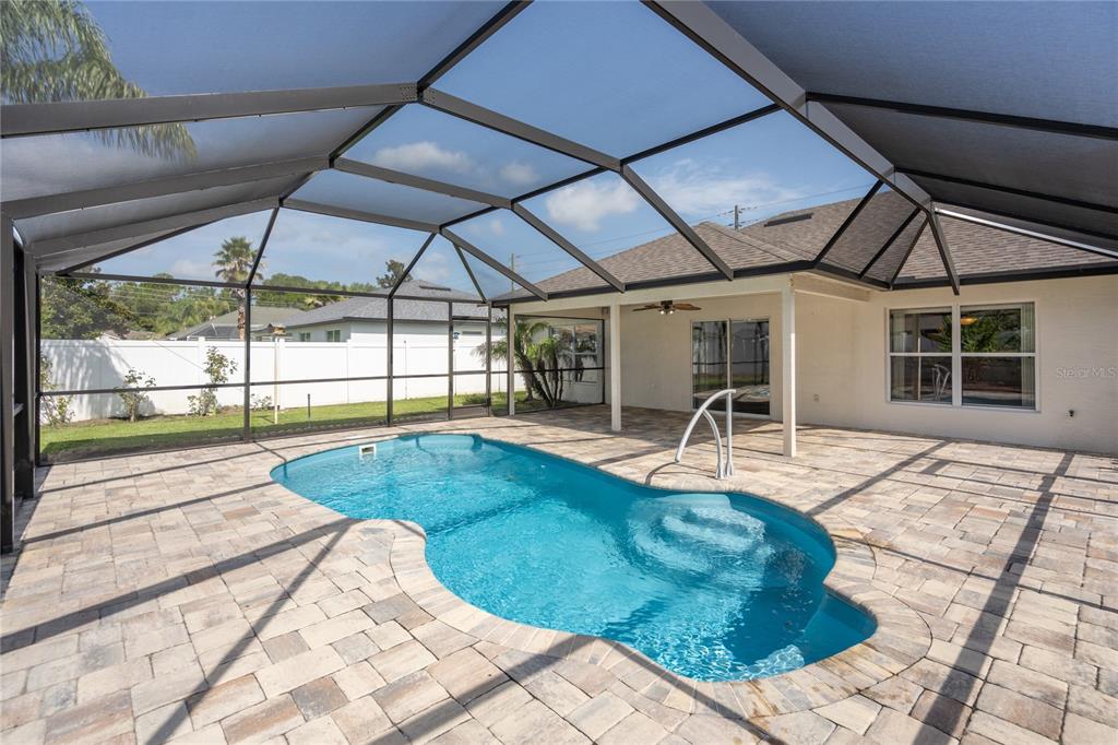 A screened-in patio features a swimming pool with steps and paver decking — 50 ROLLING SANDS DRIVE, PALM COAST, FL