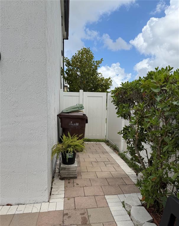 A paved side yard features a trash bin, a potted plant, and a white fence — 10306 W 33RD LANE, HIALEAH, FL