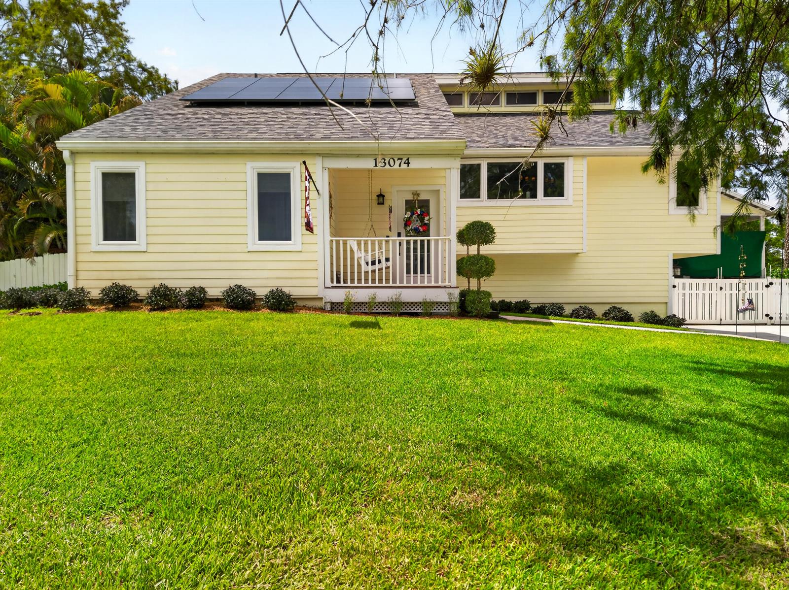 A yellow two-story house features a front porch, solar panels, and a manicured lawn — 13074 La Mirada Circle, Wellington FL 33414, WELLINGTON, FL