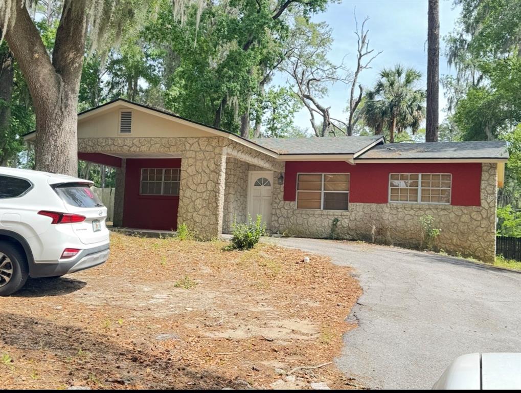 A single-story house features a stone facade, red painted accents, and a paved driveway — 1338 NE 16TH STREET, OCALA, FL