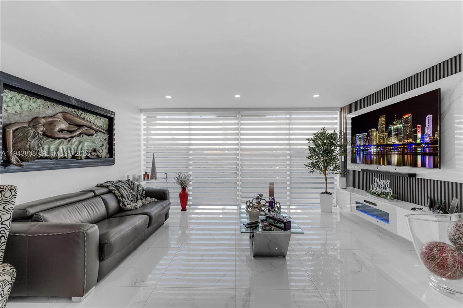 A modern living room features a dark leather sofa, a large television, and white tile flooring — 13835 SW 84th St # 503, Miami FL 33183, MIAMI, FL