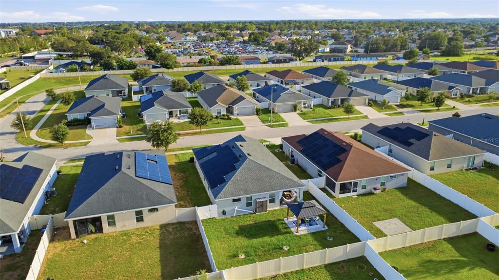 An aerial view shows suburban houses with solar panels and fenced backyards in a neighborhood — 475 MONTICELLI DRIVE, HAINES CITY, FL