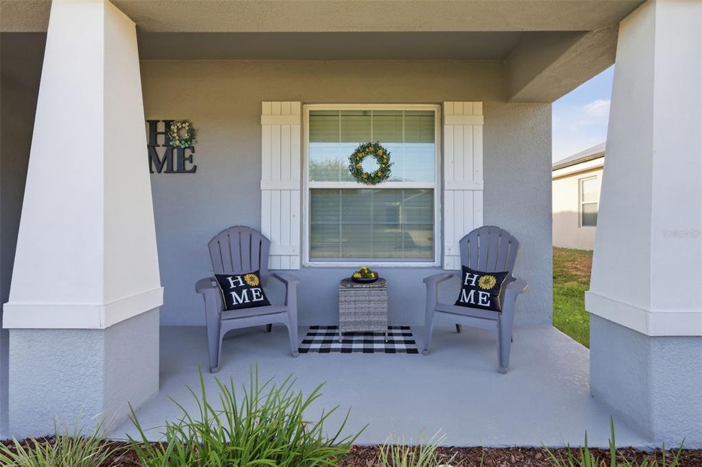 A covered front porch features two gray chairs, a small table, and decorative home signage — 475 MONTICELLI DRIVE, HAINES CITY, FL