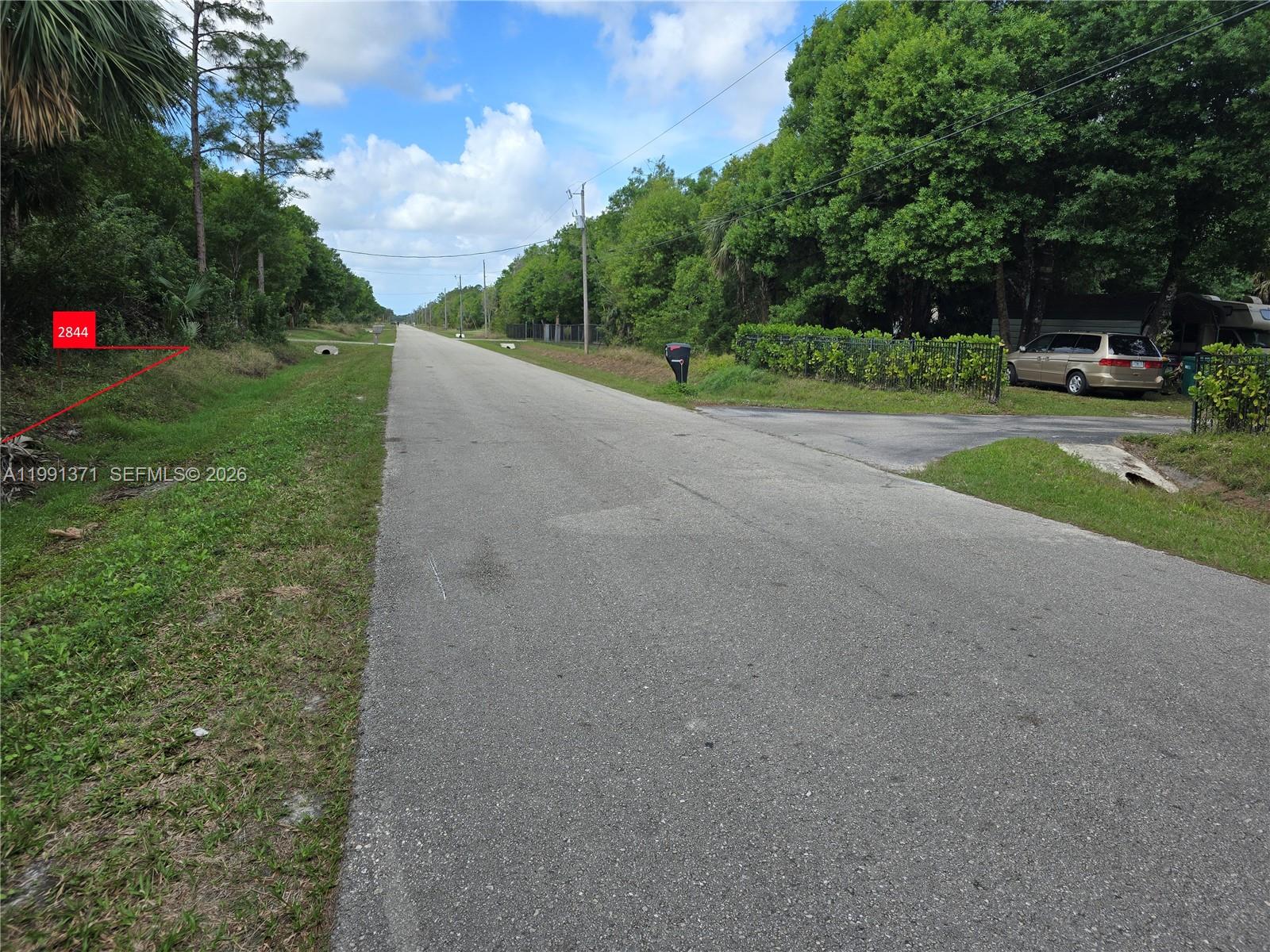A paved road runs through a wooded area with a grassy shoulder and utility poles — 2844 70th Ave NE, Naples FL 34120, NAPLES, FL