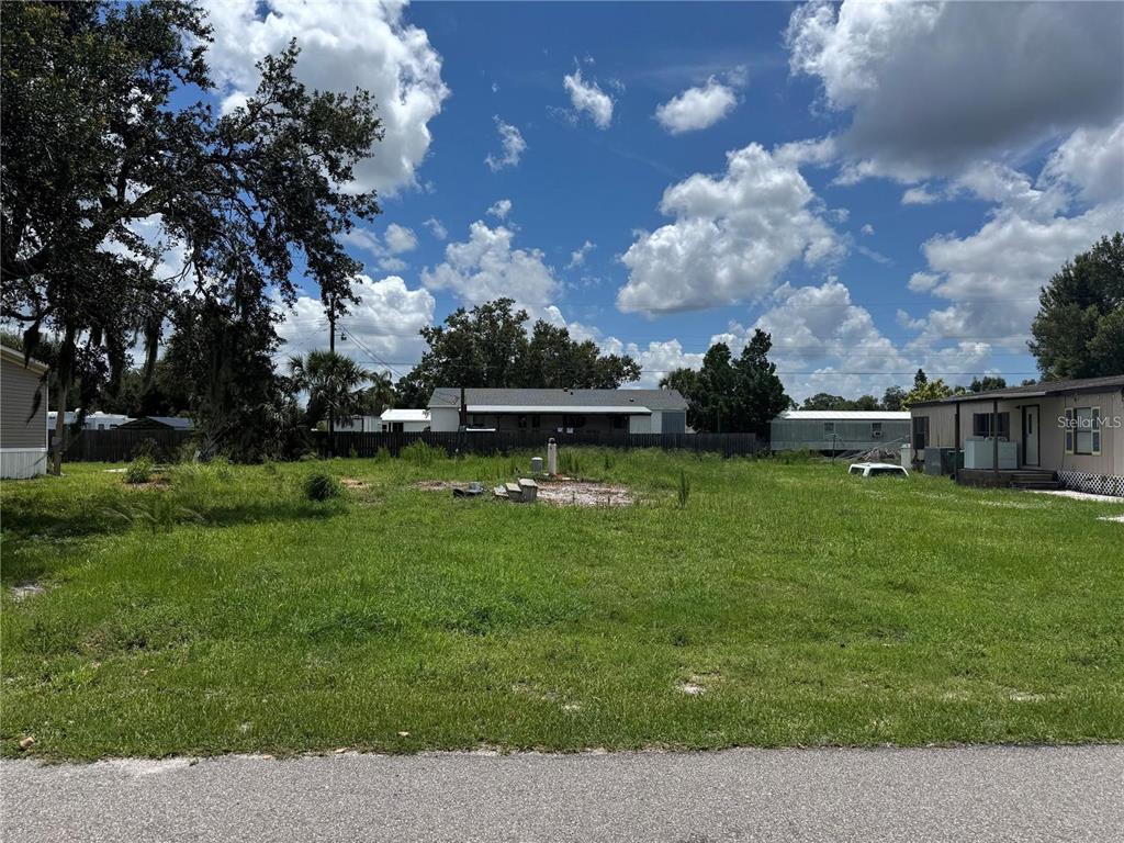 A vacant grassy lot sits between two residential structures under a blue sky with clouds — 9308 MANDY STREET, PUNTA GORDA, FL