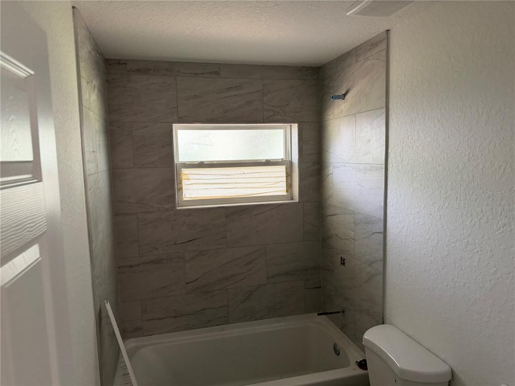 A bathroom features a white bathtub, a window, and gray tiled walls — 6 S BARBOUR STREET, BEVERLY HILLS, FL