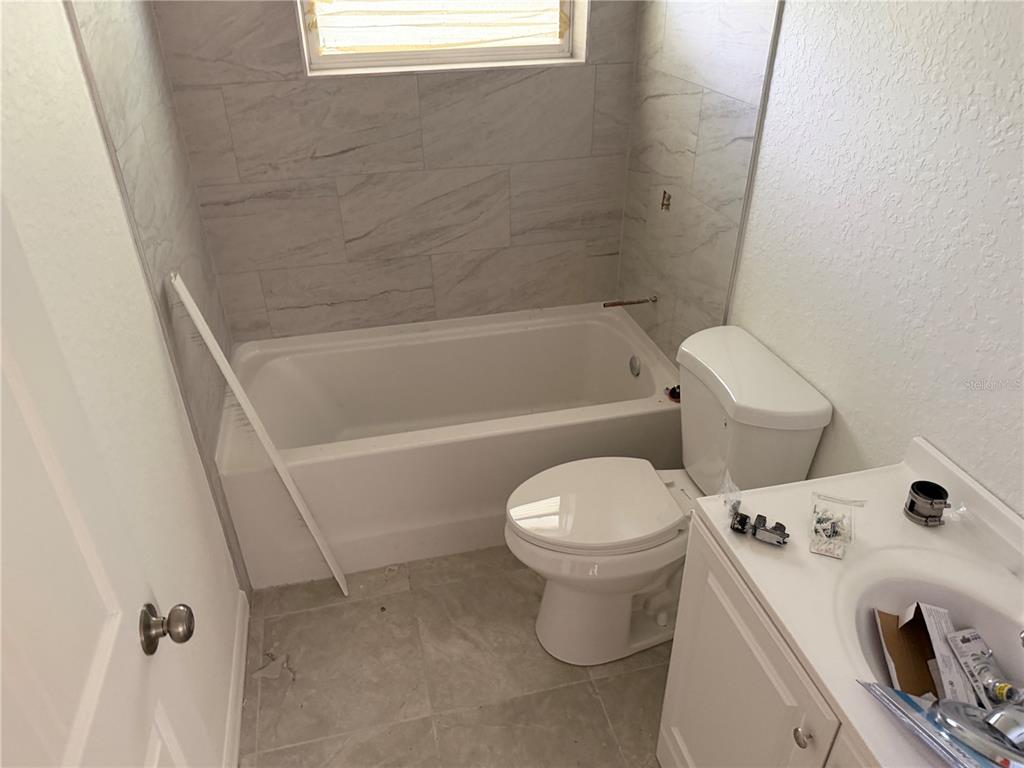 A bathroom features a white bathtub with marble-look tile walls, a toilet, and a vanity — 6 S BARBOUR STREET, BEVERLY HILLS, FL