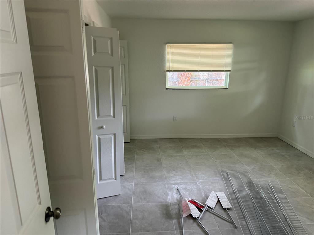 An empty bedroom features light gray tile flooring, white walls, and a closet with bifold doors — 6 S BARBOUR STREET, BEVERLY HILLS, FL