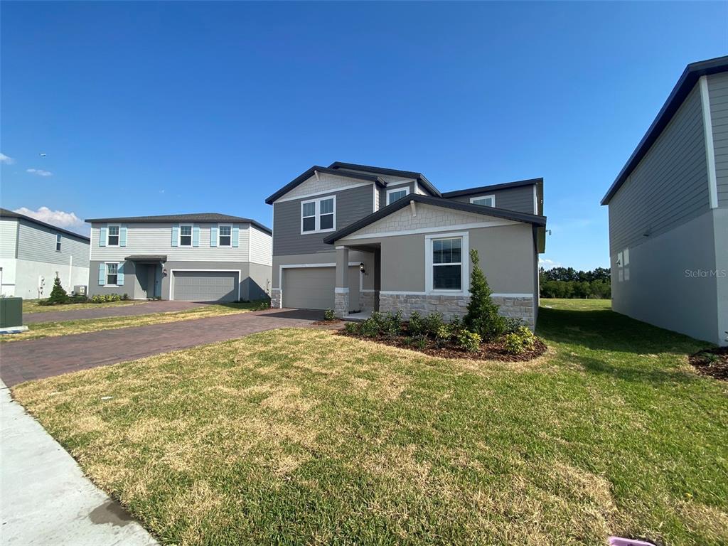 A two-story suburban house with a gray and tan exterior, stone accents, and a driveway — 461 WHISTLING DUCK TRAIL, ST CLOUD, FL