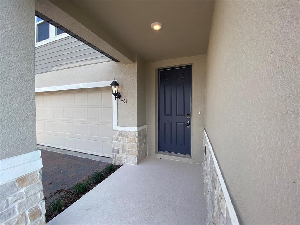 A covered entryway features a dark blue front door, stone accents, and a garage door — 461 WHISTLING DUCK TRAIL, ST CLOUD, FL