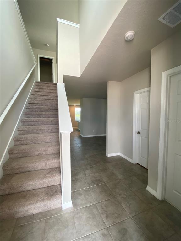 A carpeted staircase leads to an upper level in an entryway with tiled flooring — 461 WHISTLING DUCK TRAIL, ST CLOUD, FL