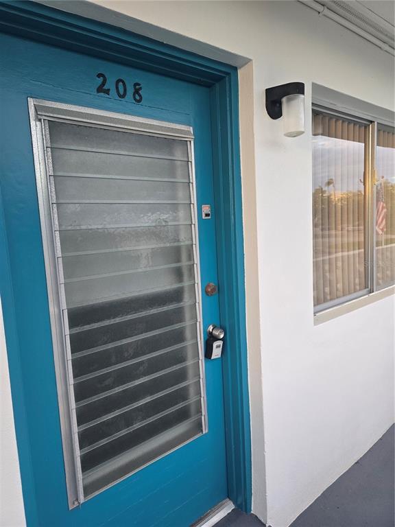 A teal door with a louvered glass window and a lockbox sits beside a window — 8220 112TH STREET UNIT 208, SEMINOLE, FL