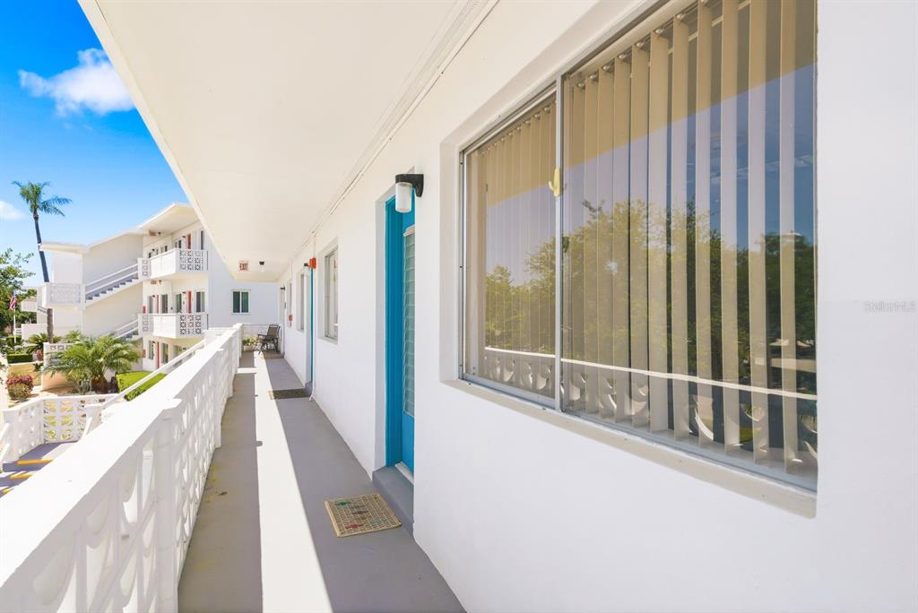An outdoor walkway with a white railing leads past a blue door and window — 8220 112TH STREET UNIT 208, SEMINOLE, FL