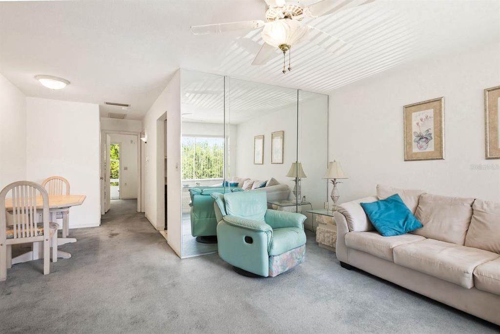A living room with gray carpet, a beige sofa, a teal armchair, and mirrored walls — 8220 112TH STREET UNIT 208, SEMINOLE, FL